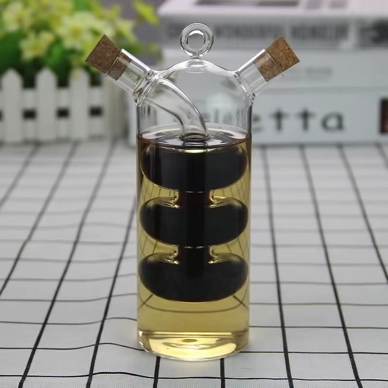 A transparent glass interlocking oil and vinegar bottle with cork stoppers and dual dispensers, containing oil and vinegar.